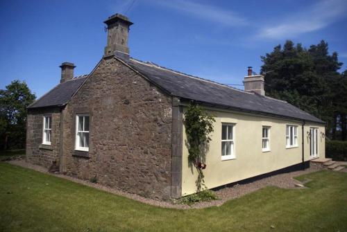 una antigua casa de piedra con un patio de césped en Lake Cottage , Middleton Hall Estate en Smeafield