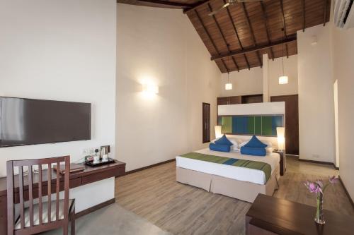 a bedroom with a bed and a desk and a tv at The Calm Resort & Spa in Pasikuda