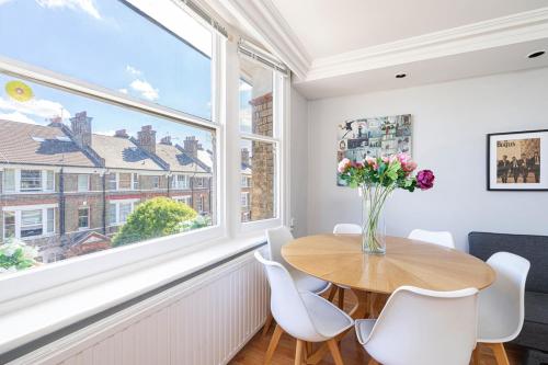 ein Esszimmer mit einem Tisch, Stühlen und einem Fenster in der Unterkunft JOIVY Bright apt in West Hampstead in London