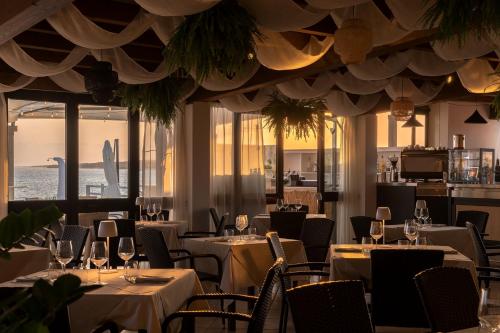 un restaurant avec des tables blanches, des chaises et des fenêtres dans l'établissement Hotel da Cesare Maluentu, à Putzu Idu
