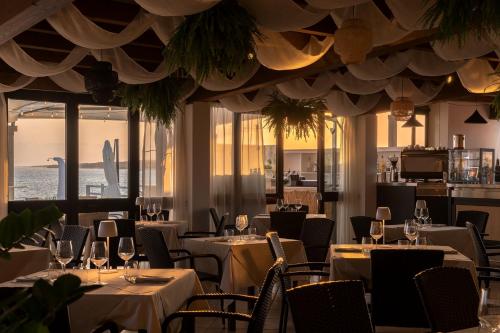 a restaurant with white tables and chairs and windows at Hotel da Cesare Maluentu in Putzu Idu