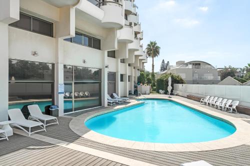 een zwembad in een hotel met stoelen en een gebouw bij Elegant Beachfront Duplex with Private Parking in Herzelia 