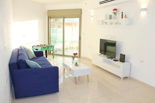 a living room with a blue couch and a tv at Beach Suite Israel - Indoor Pool, Best View, Gym, Massage Chair, Spa ביץ סוייט ישראל - נוף ים מאלף, בריכה מקורה, כיסא מסאז, חדר כושר וספא in Ashqelon