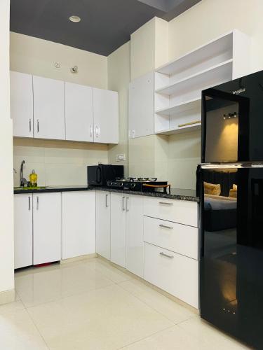 a kitchen with white cabinets and a black refrigerator at Serviced Apartment near Medanta by BedChambers in Gurgaon