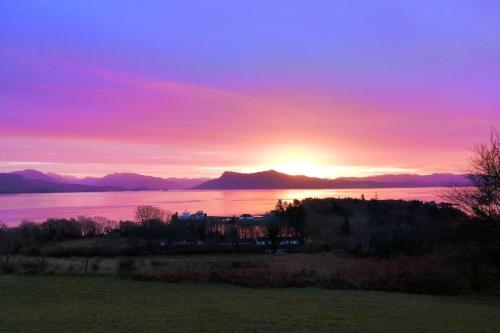 una puesta de sol sobre el agua con montañas en el fondo en Armadale Castle Cabins, en Ardvasar