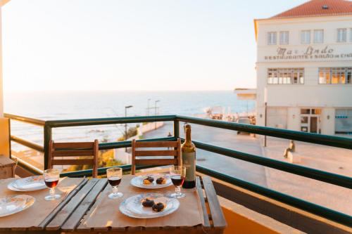 a table with a bottle of wine and glasses on a balcony at Alfaiate Beach House in Santa Cruz