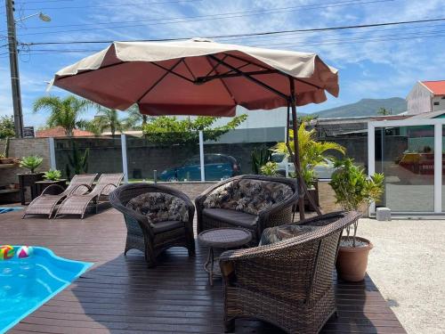 een patio met stoelen en een parasol naast een zwembad bij Pousada da Mel - Canasvieiras Floripa in Florianópolis