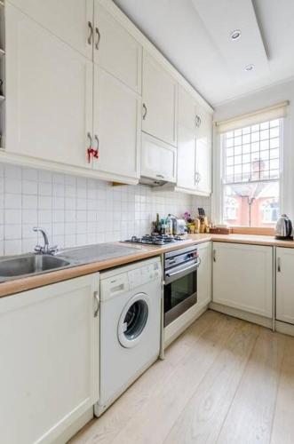 a kitchen with white cabinets and a sink and a dishwasher at Flat cannot be booked in London