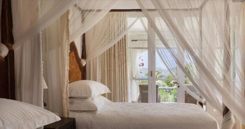 a bedroom with a white canopy bed with a window at Breathtaking 6 BR Villa with Infinity Pool in Pointe Milou