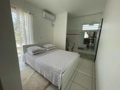 a white bedroom with a bed and a bathroom at L’Eucalyptus in Sainte-Rose