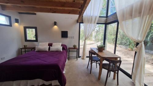 1 dormitorio con cama morada, mesa y sillas en Cabaña del Cedro Azul, San Lorenzo en Salta