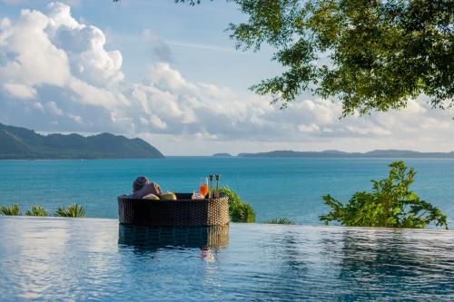 a person is sitting in a pool near the ocean at 悬崖别墅 无边海景 直达海滩 五卧泰式独栋私人泳池别墅 超漂亮日出 in Phuket Town