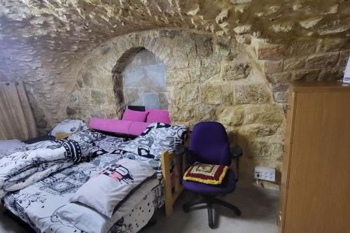 um quarto com uma parede de pedra, uma cama e uma cadeira. em historic luxury cave em Jerusalém