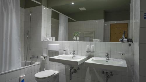 uma casa de banho com 2 lavatórios, um WC e um espelho. em Gletscher-Hotel Morteratsch em Pontresina