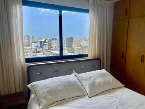 a bed with a view of a city from a window at Downtown Luxury Apt Naco: 2br 2ba in Santo Domingo