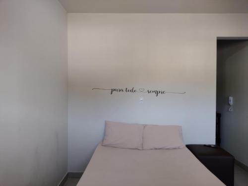 a white bed in a room with a sign on the wall at kitnet Ragnarok in Barão de Cocais