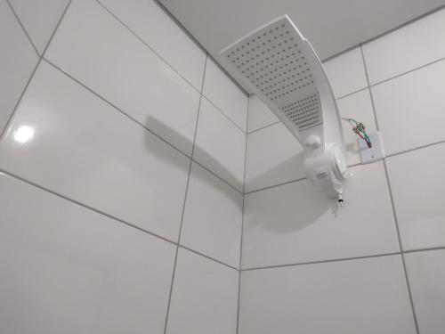 a white shower head on a white tiled wall at kitnet RAGNAROK in Barão de Cocais