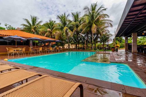 a large blue swimming pool with chairs and palm trees at Carpe Diem Eco Resort & SPA in Olímpia
