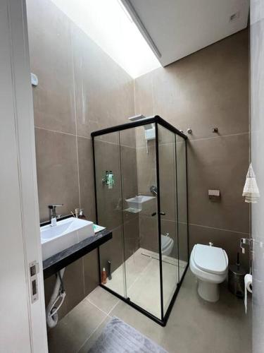 La salle de bains est pourvue d'une douche en verre et de toilettes. dans l'établissement Casa com piscina e área gourmet com churrasqueira integrada, à Maringá