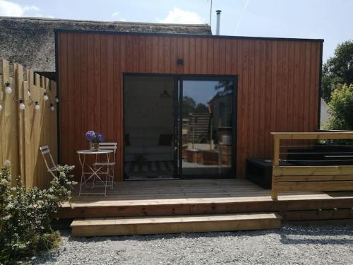ein Haus mit einer Holzterrasse mit einem Tisch in der Unterkunft Studio Les petites poules in Saint-Lyphard