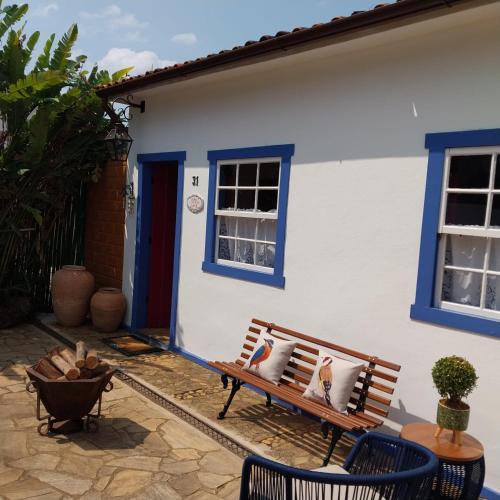 a bench in front of a white house with blue windows at Chafariz Por Um Triz Pousada de Charme in Tiradentes
