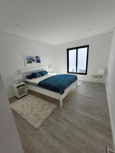 a white bedroom with a bed and a window at Casa das Azorinas in Fenais da Luz