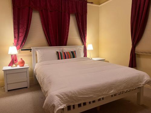 1 dormitorio con 1 cama blanca grande y cortinas rojas en Redgum Cottage, en Mudgee