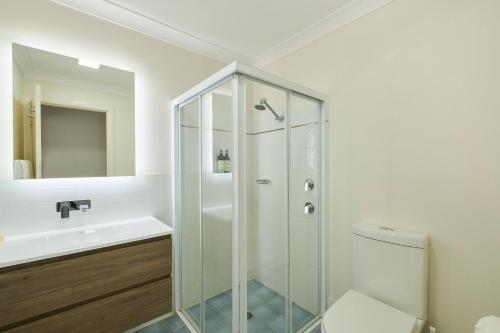 a bathroom with a shower and a toilet and a sink at Flynns on Surf Beach Villas in Port Macquarie
