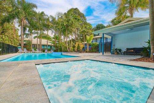 a swimming pool in front of a house with palm trees at Flynns on Surf Beach Villas in Port Macquarie
