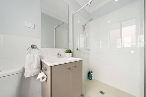 a white bathroom with a sink and a shower at The Seachange - Brand New, Beachy Family Retreat. in Ettalong Beach