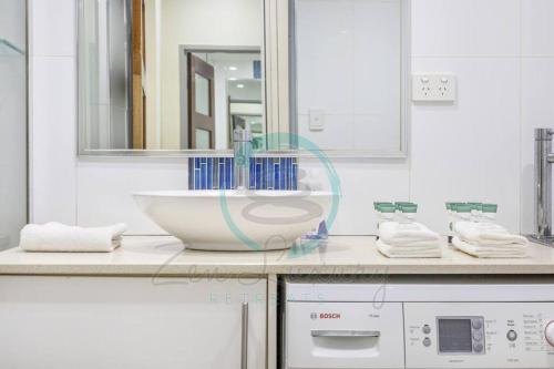 a white bathroom with a sink and a mirror at Zen by the Coast: 2-BR Cozy Retreat Near Uni/Shops in Casuarina