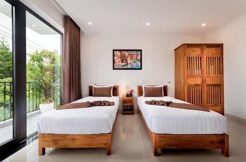 two beds in a room with a window at Tomorrow Boutique Villa Hoi An in Hoi An