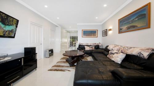 a living room with a leather couch and a table at Castaway - Ettalong Beach in Ettalong Beach