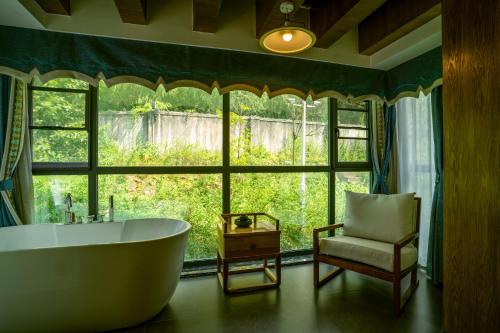 a bathroom with a tub and a chair and a window at 张家界惹莲心栖墅·精品民宿 in Zhangjiajie