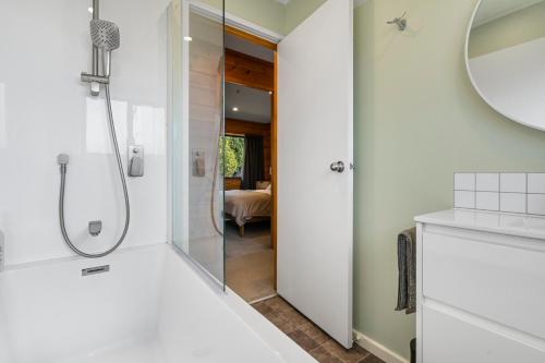 baño blanco con ducha y espejo en Sunset Cottage - Waikanae Beach Holiday Home, en Waikanae