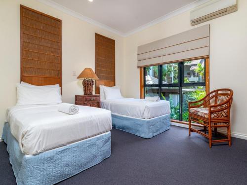 two beds in a room with a chair and a window at The Point Villa 10 in Port Douglas