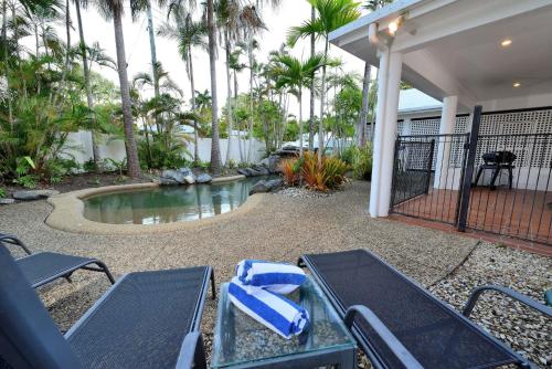 a patio with chairs and a pool with palm trees at Coral Drive Retreat in Port Douglas