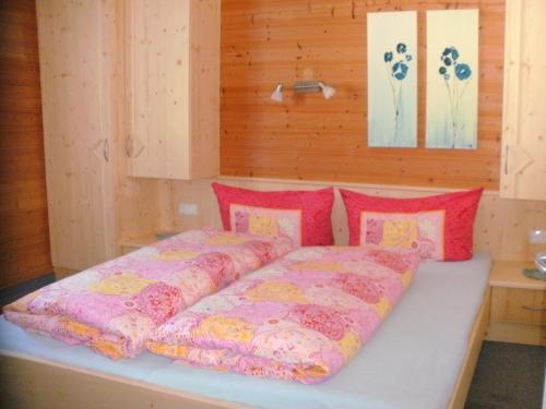 Cama en habitación con almohadas rojas y rosas en Ferienwohnungen Reinalter, en Kappl