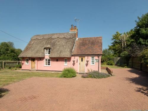 une maison rose avec toit sur une cour de terre dans l'établissement Two Bedroom Grade ll Cottage At AZ Luxury Stays Honey Horsefield With WiFi And Free Parking, à Hundon