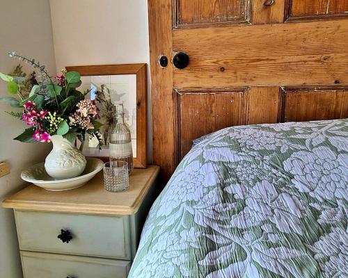 a bed with a table with a vase of flowers on it at Finest Retreats - Ingleside Cottage in Whitby