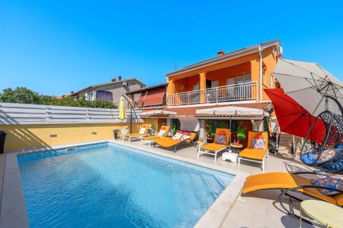 a swimming pool with chairs and umbrellas next to a building at Venus Holiday House with Pool in Banjole