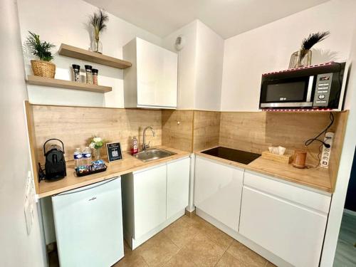 a small kitchen with white cabinets and a microwave at Perle rare « Le Cosy de CDG » in Le Blanc-Mesnil