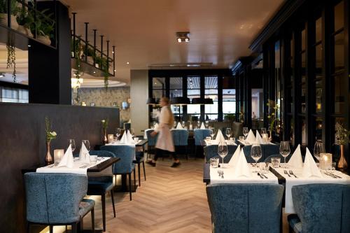 uma sala de jantar com mesas e cadeiras brancas e uma mulher em Van der Valk Hotel 's-Hertogenbosch – Vught em Den Bosch