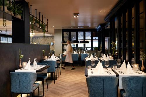 a dining room with white tables and chairs and a woman at Van der Valk Hotel 's-Hertogenbosch – Vught in Den Bosch