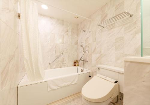 a white bathroom with a toilet and a bath tub at Kanazawa New Grand Hotel Premier in Kanazawa