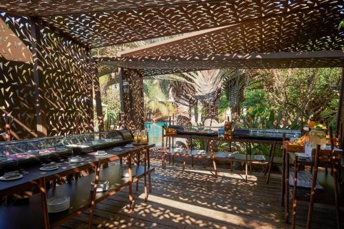 Un patio con mesas y sillas y árboles al fondo. en Lopesan Baobab Resort, en Meloneras