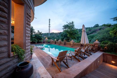 an outdoor swimming pool with chairs and a umbrella at The Almond Tree in Jodhpur