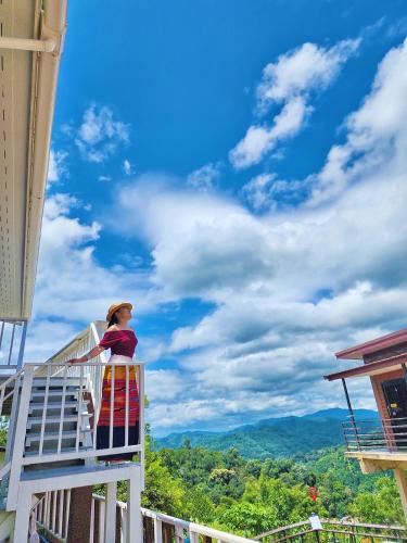 a woman standing on a balcony looking at the mountains at ดอยตุง สันติสุขโฮมสเตย์ in Ban Pa Kluai La Hu