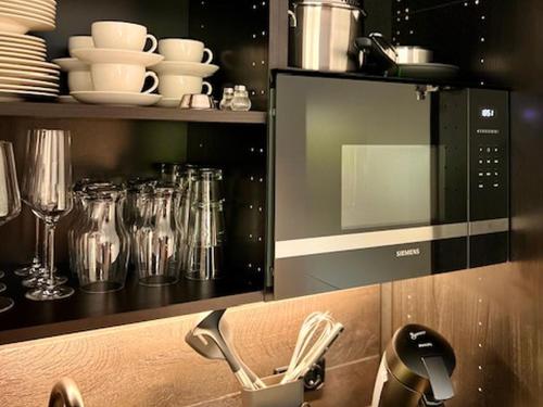 a microwave in a kitchen with glasses and dishes at ROSER Suiten in Gengenbach