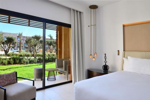 a bedroom with a bed and a chair and a balcony at Hilton Taghazout Bay Beach Resort & Spa in Taghazout